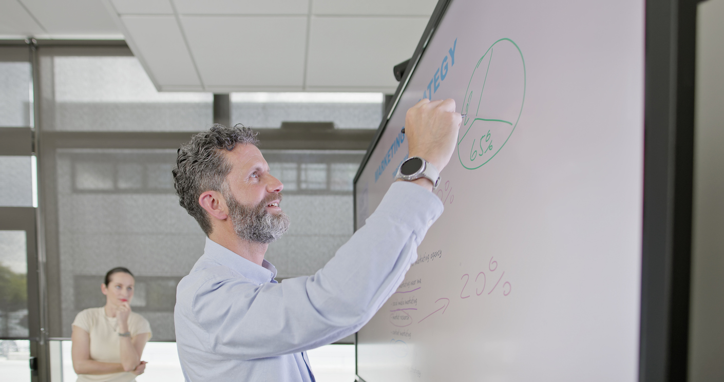 Executive pointing to a strategic digital marketing growth flywheel diagram on a boardroom glass wall.
